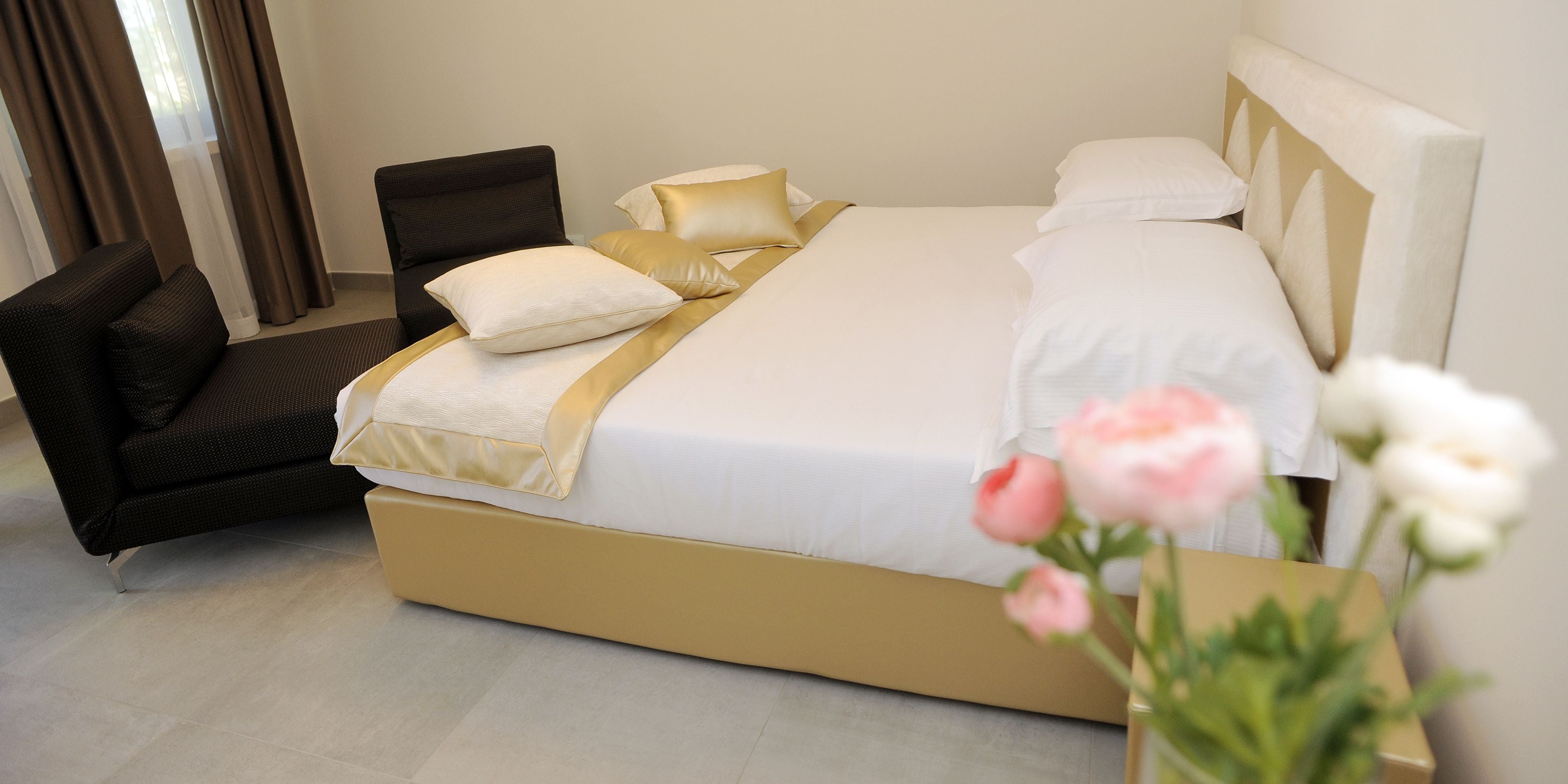 Habitación de hotel con una cama grande, una silla y un florero con flores.