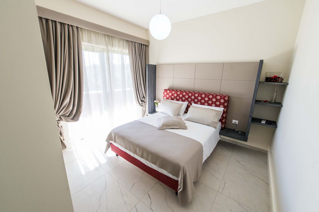 Et moderne hotelværelse med en stor seng, en sengegavl med et mønstret design, et natbord med en lampe og en indbygget hylde med dekorative genstande.
