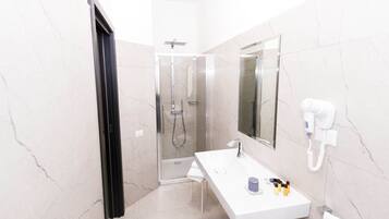 Un baño moderno con ducha de vidrio, un lavabo blanco con espejo y un secador de pelo en la pared.