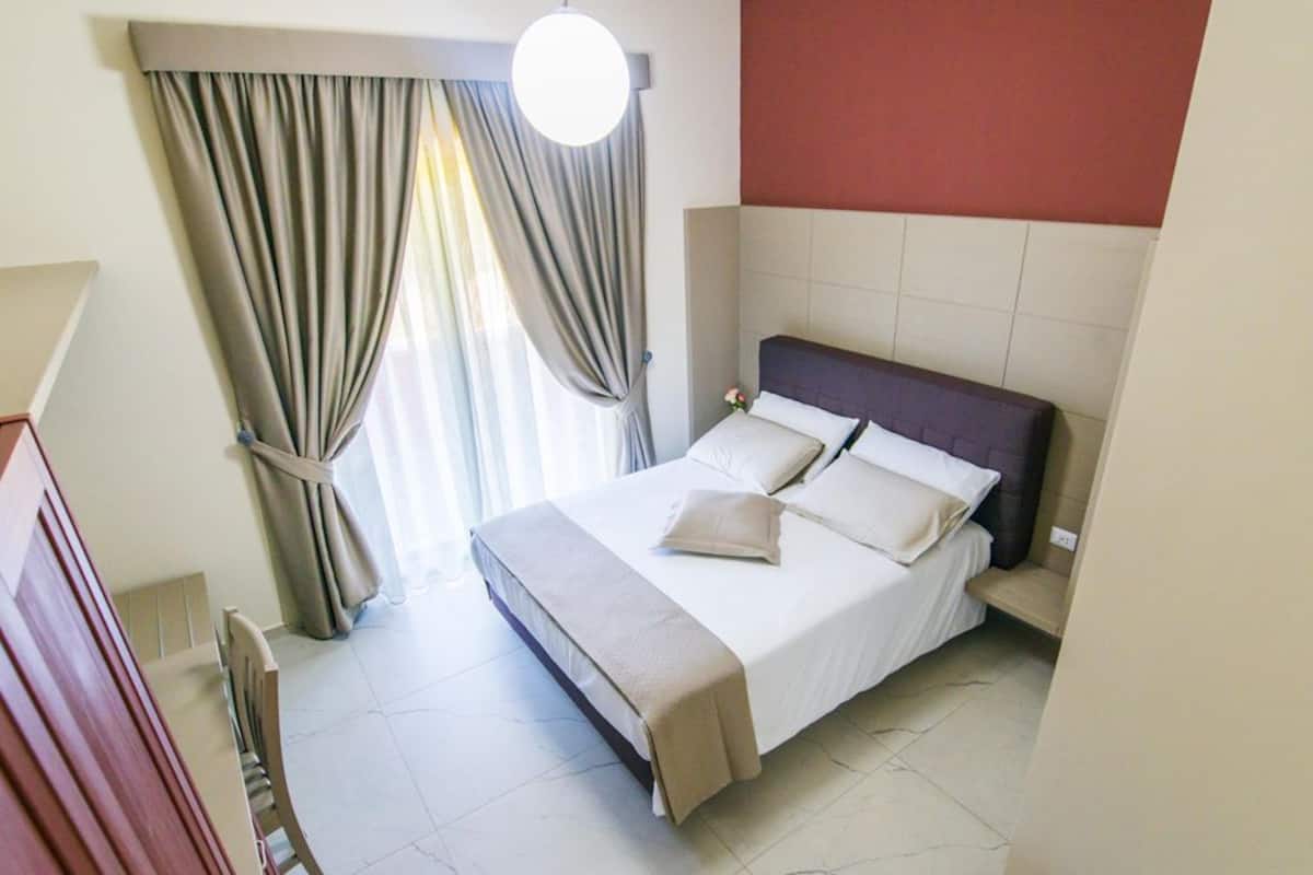 A hotel room with a bed, curtains, a bedside table, and a hanging light fixture.
