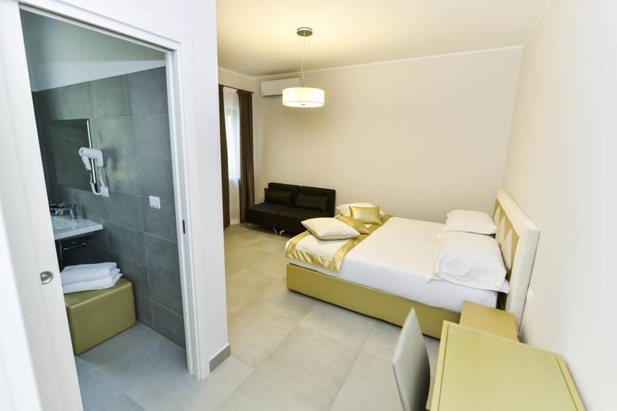 A modern hotel room with a large bed, a bedside table, a desk, and a shower area.