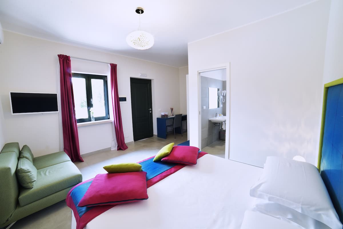 A hotel room with a bed, a green sofa, a desk, and a bathroom visible through an open door.