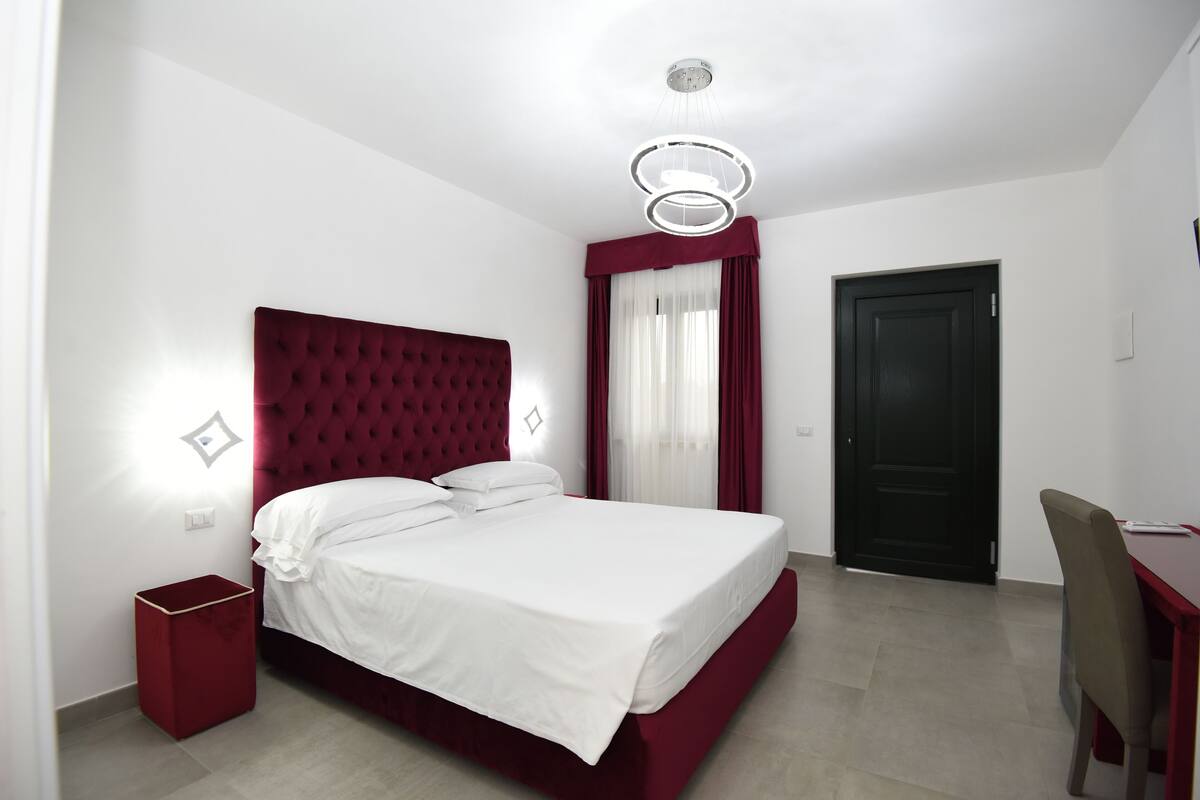 A hotel room with a large bed, a desk, and a door.
