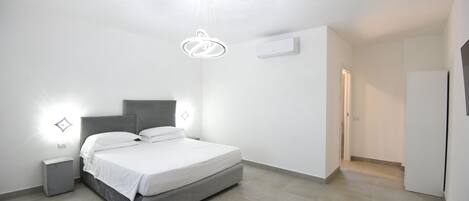 Un dormitorio moderno con cama, mesitas de noche, lámpara colgante y una puerta que da a otra habitación.