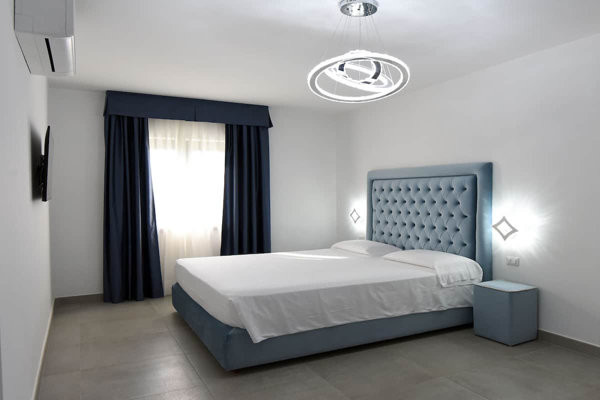 A modern bedroom with a large bed, a bedside table, a wall-mounted TV, and a ceiling light fixture.