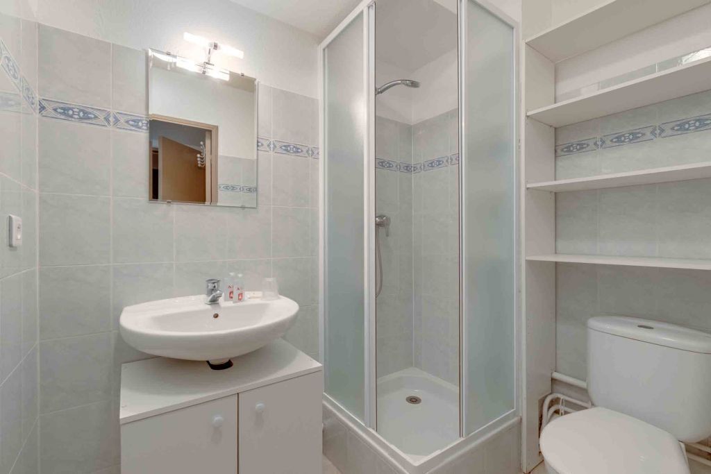 Ein Badezimmer mit Waschbecken, Spiegel, Duschkabine, Toilette und Ablagefächern.
