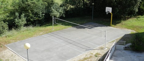 Ulkokenttä, jossa on tenniskenttä ja verkko, ja sitä ympäröivät puut sekä koripallokehä.