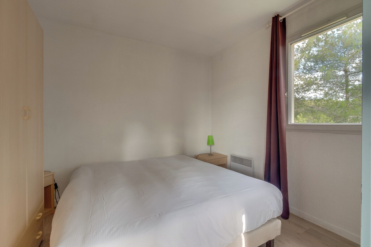 A bedroom with a bed, a nightstand, a lamp, and a window with curtains.