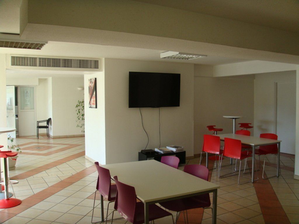 A conference room with a large table, red chairs, a flat-screen TV, and a tiled floor.