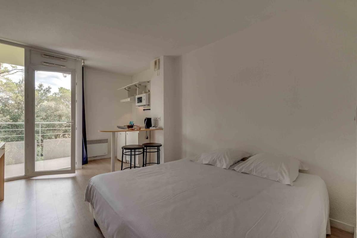 Ein Schlafzimmer mit einem großen Bett, einem Schreibtisch mit Stuhl und einer Schiebetür zum Balkon.