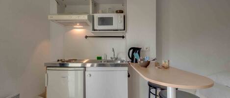 Una kitchenette compacta equipada con microondas, un refrigerador pequeño, un lavamanos y un taburete de bar.
