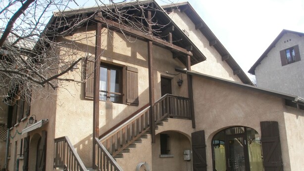 A two-story building with a wooden staircase, arched doorways, and a balcony.