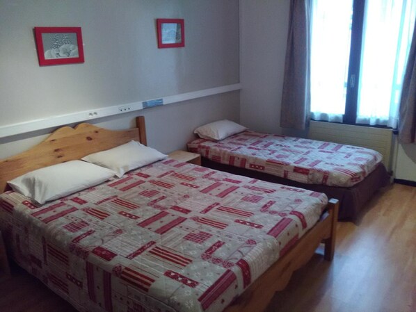 A room with two single beds, each with a patterned bedspread, a wooden headboard, and a white pillow. There are two framed pictures on the wall above the beds.