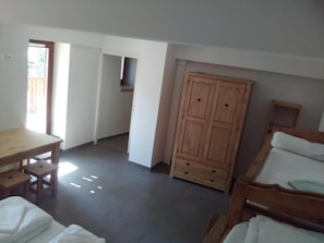 Ein Zimmer mit einem Holztisch, einem Kleiderschrank und einem Bett mit weißer Bettwäsche.
