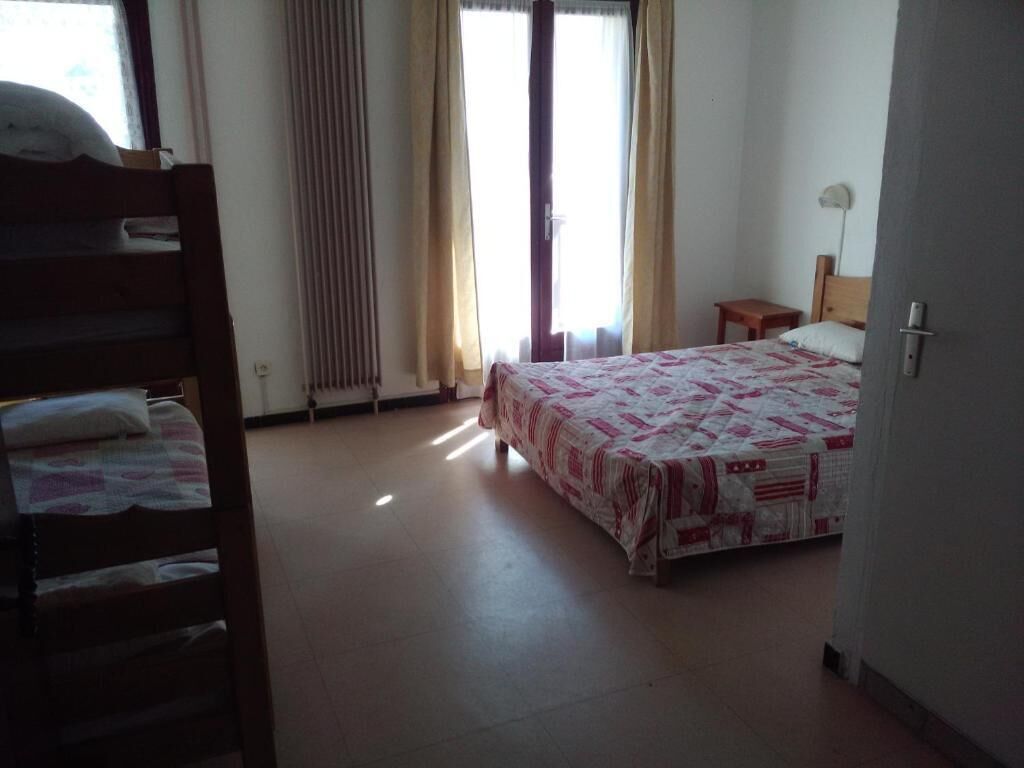 A bedroom with a bed, a wooden bench, a small table, and a window with curtains.