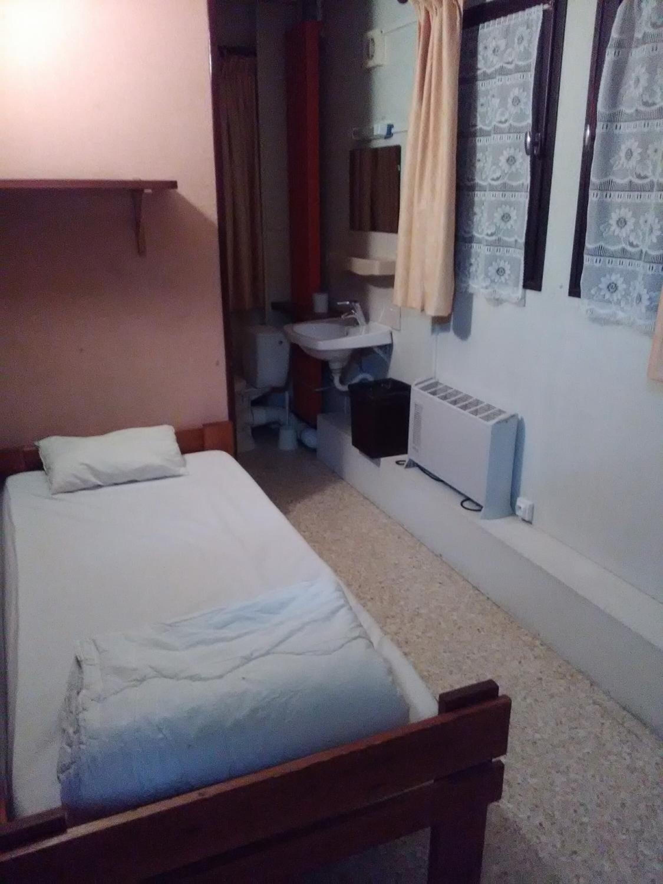 A small, simple room with a single bed, a small desk, and a radiator.