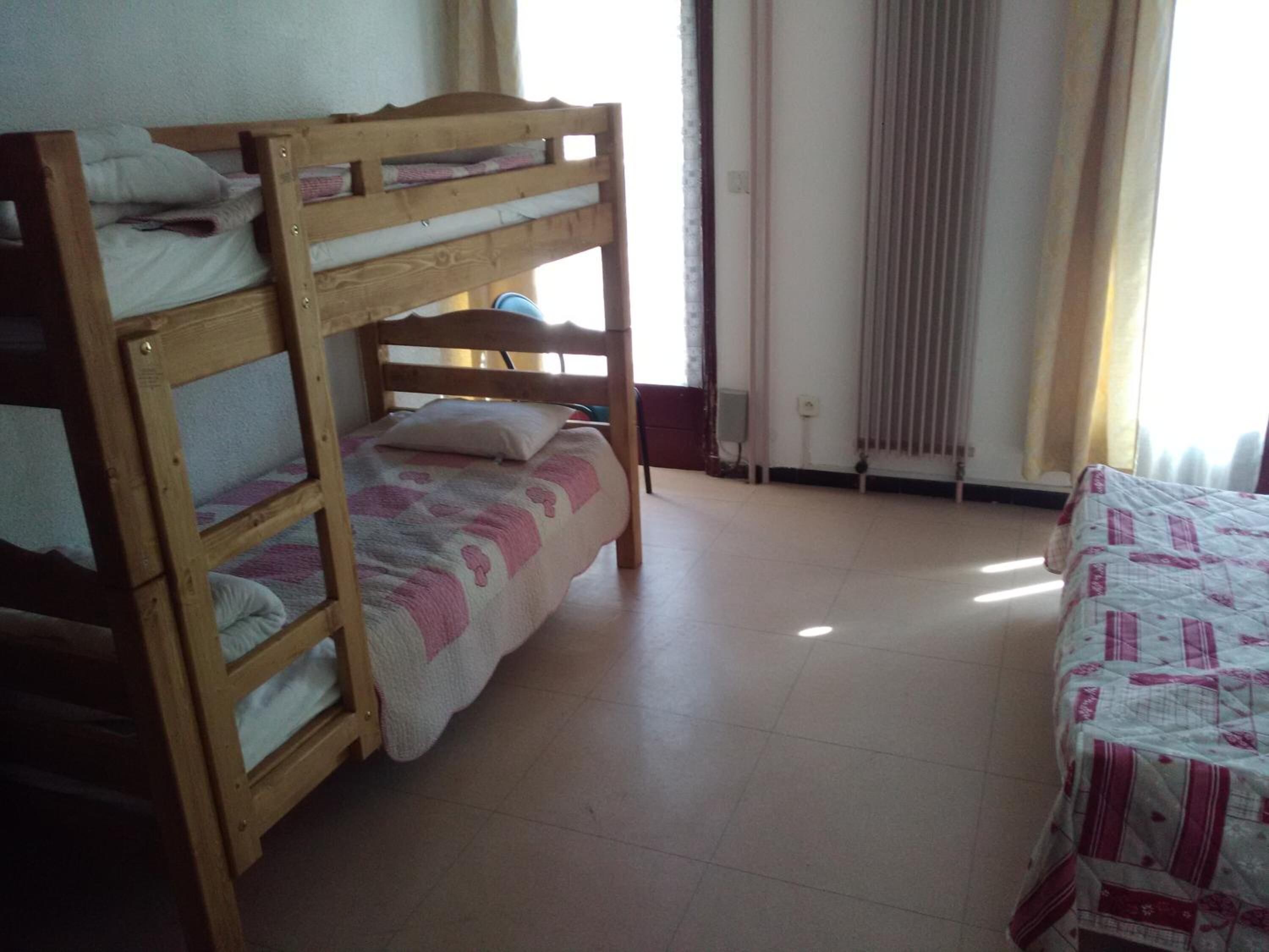 Dormitorio con literas, ventana, radiador y cama con edredón estampado.