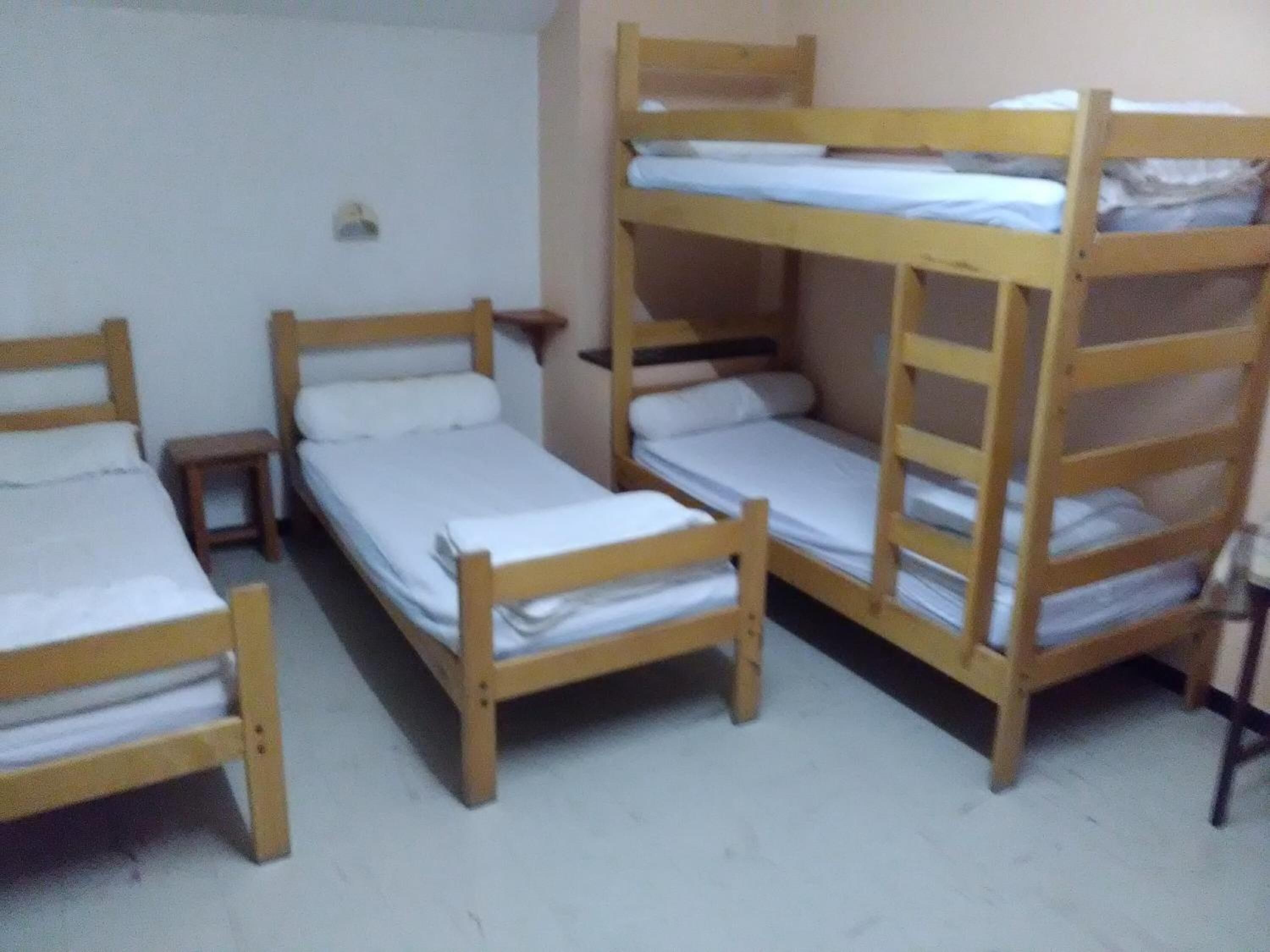 A dormitory room with bunk beds and a small bedside table.