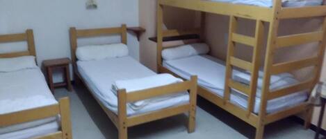 A dormitory room with bunk beds and a small bedside table.
