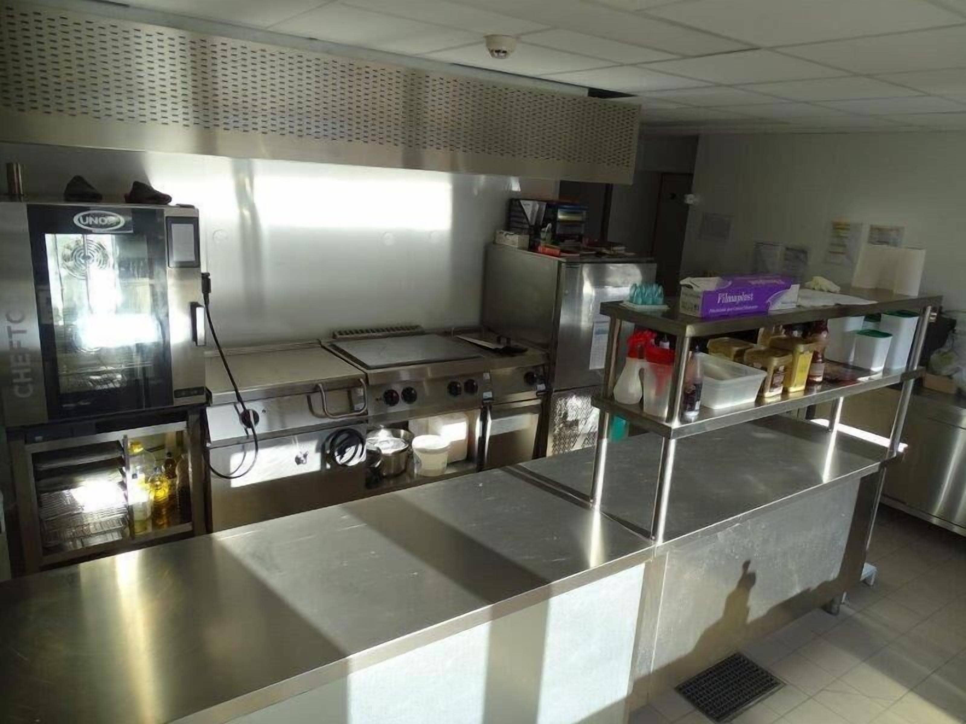 Une cuisine professionnelle équipée d’appareils en acier inoxydable, notamment une friteuse, une plaque de cuisson et un fourneau à plusieurs brûleurs.