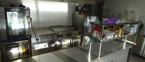 Une cuisine professionnelle équipée d’appareils en acier inoxydable, notamment une friteuse, une plaque de cuisson et un fourneau à plusieurs brûleurs.