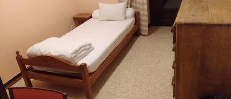 A small, single-bed room with a wooden headboard, a bedside table, and a wooden dresser.