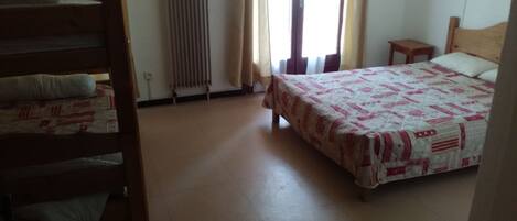 A bedroom with a bed, a wooden chair, a radiator, and a window with curtains.