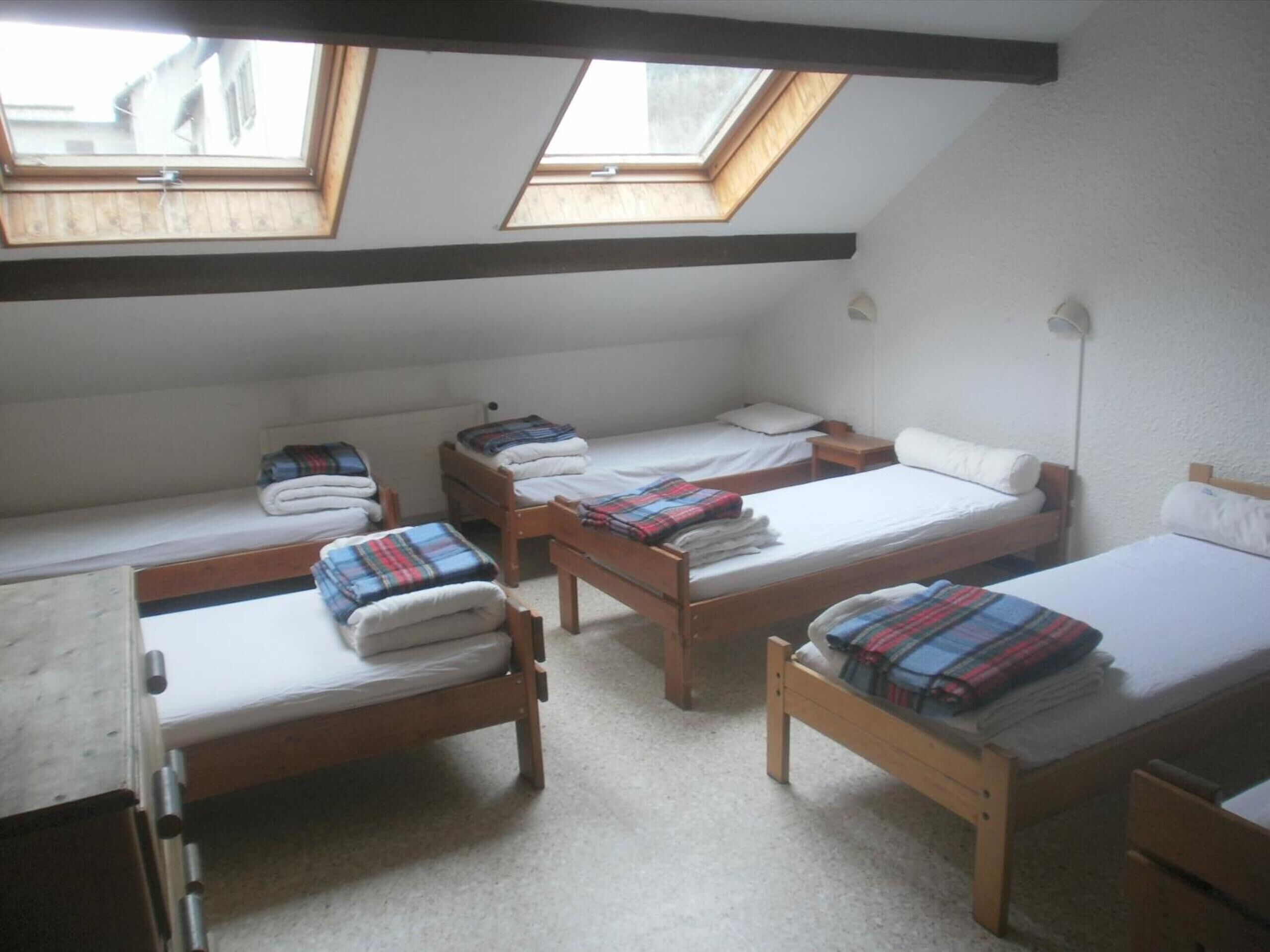 A dormitory room with four wooden beds, a desk, and two skylights.