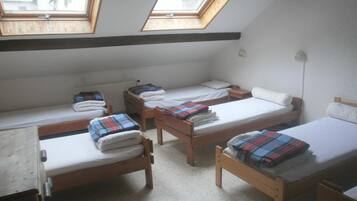 A dormitory room with four wooden beds, a desk, and two skylights.