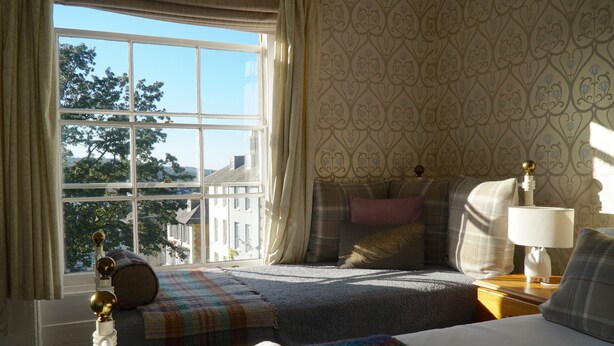 A bedroom with a large window, a bed, a bedside table with a lamp, and a patterned wall. - Castle Guest House (Dover)