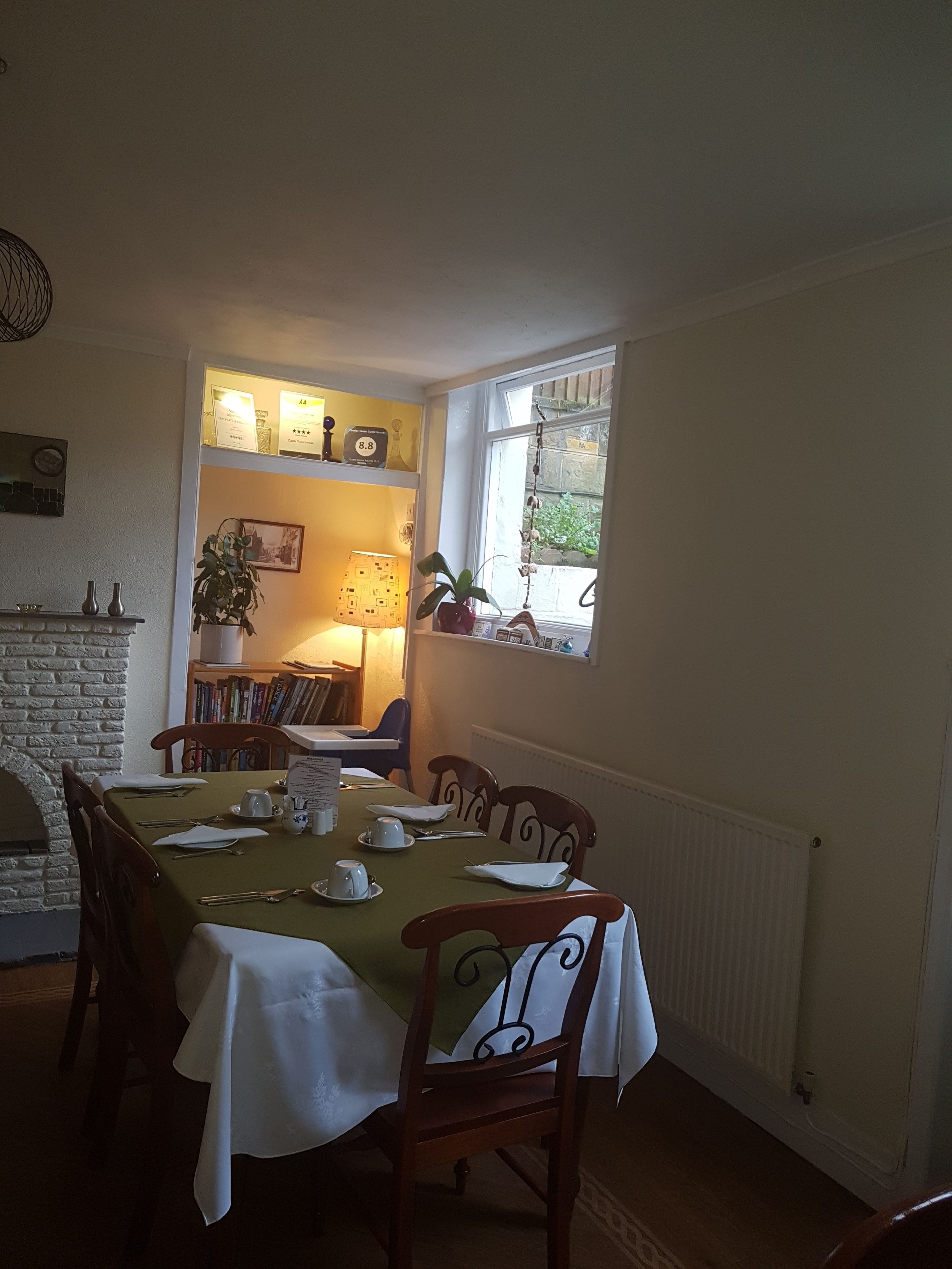 Ein Esszimmer mit einem Tisch für sechs Personen, einem Kamin aus Ziegelsteinen und einem Fenster mit Blick ins Grüne.