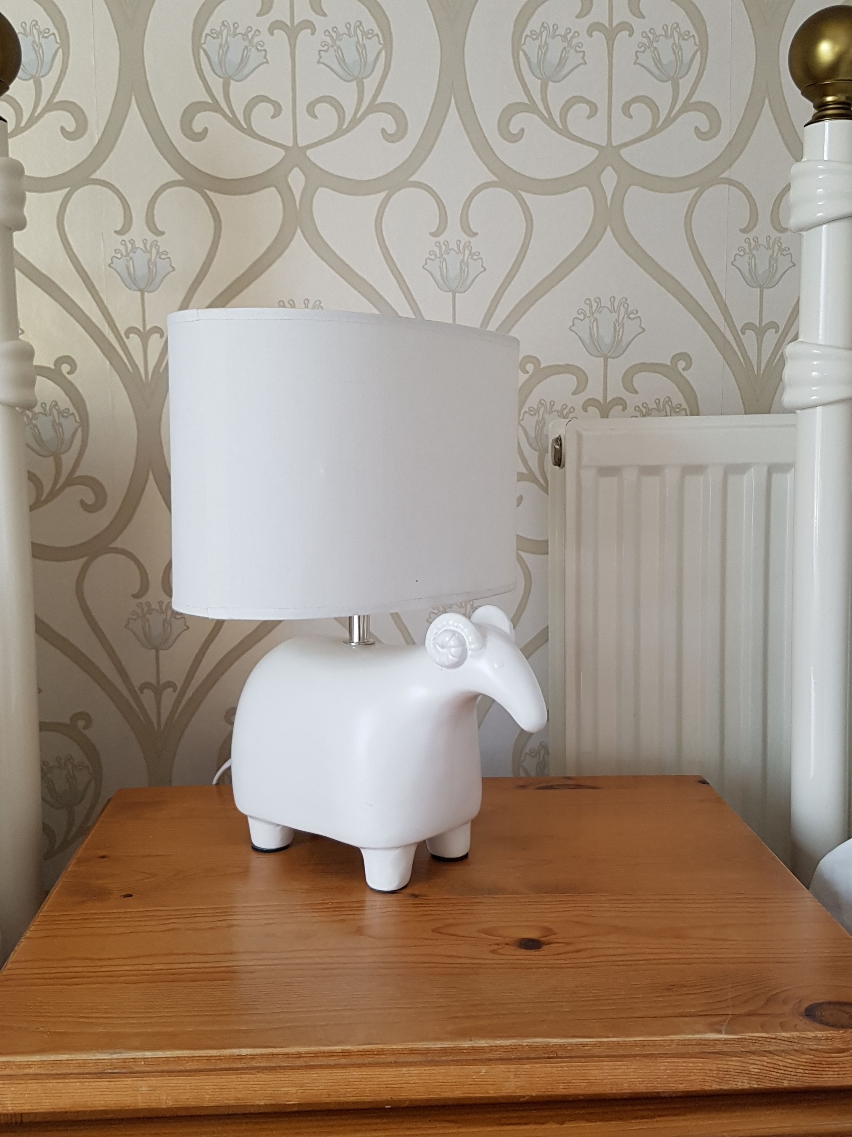 A white lamp with an elephant head on a wooden table against a wallpapered wall.