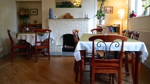 A dining room with a white brick fireplace, wooden chairs, a table with a white tablecloth, and bookshelves filled with books. - Castle Guest House (Dover)