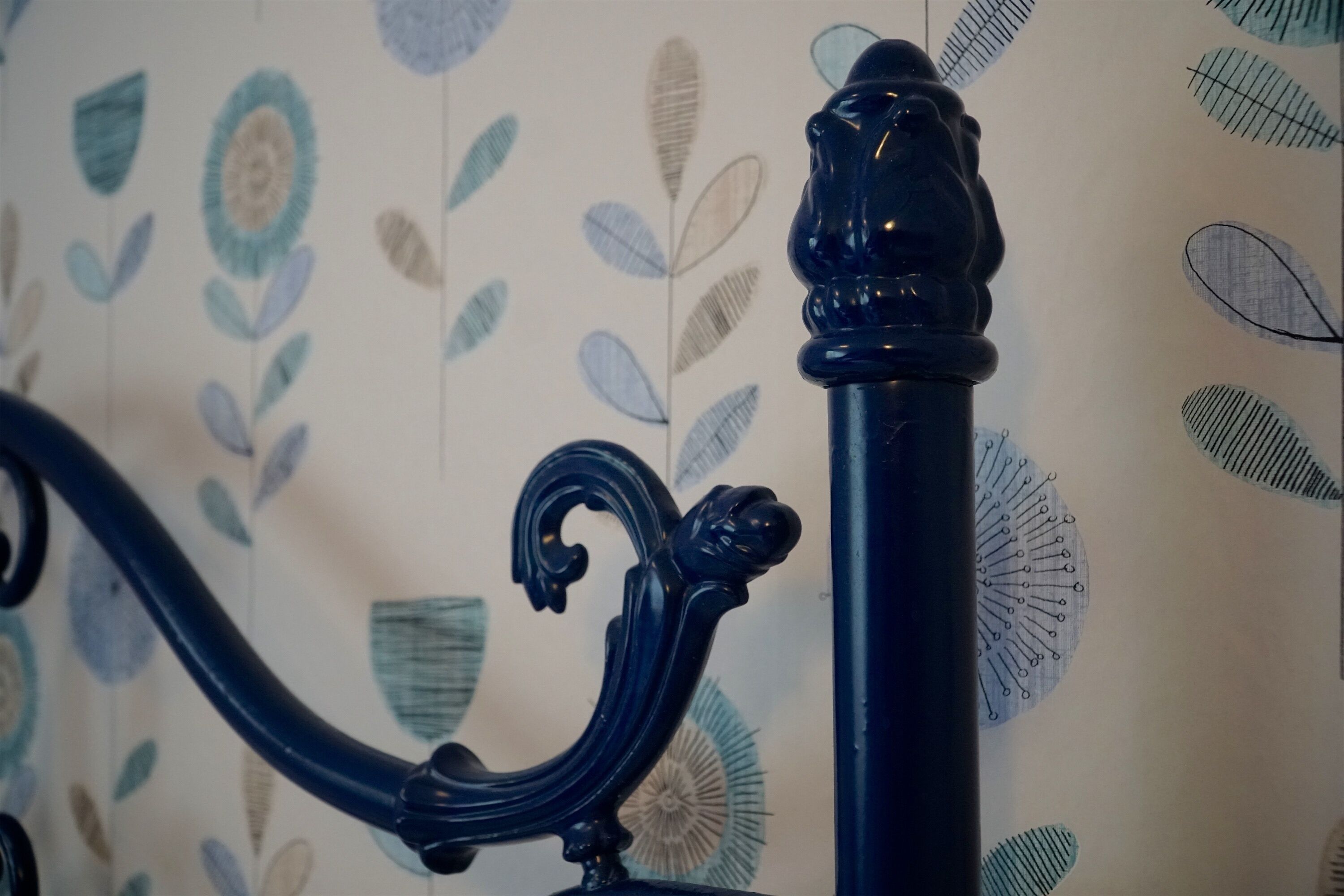 Una struttura letto in metallo nero con decorazioni elaborate, su uno sfondo con motivo floreale.