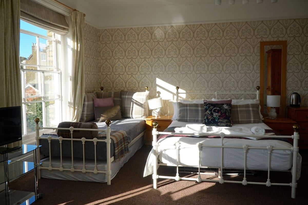 A bedroom with two beds, a TV, and a window with curtains.