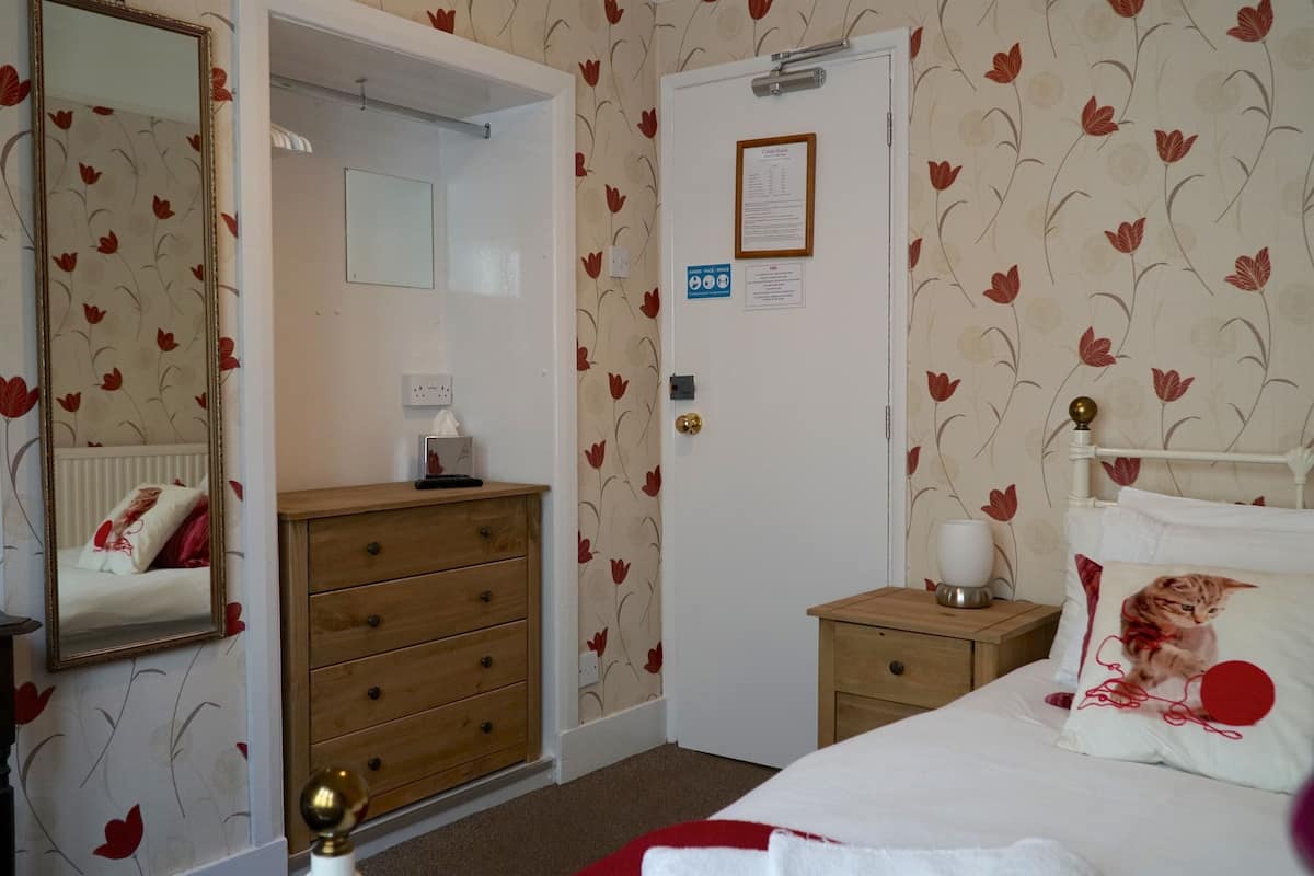 A bedroom with a bed, a dresser, a nightstand, a mirror, and a door with a sign.