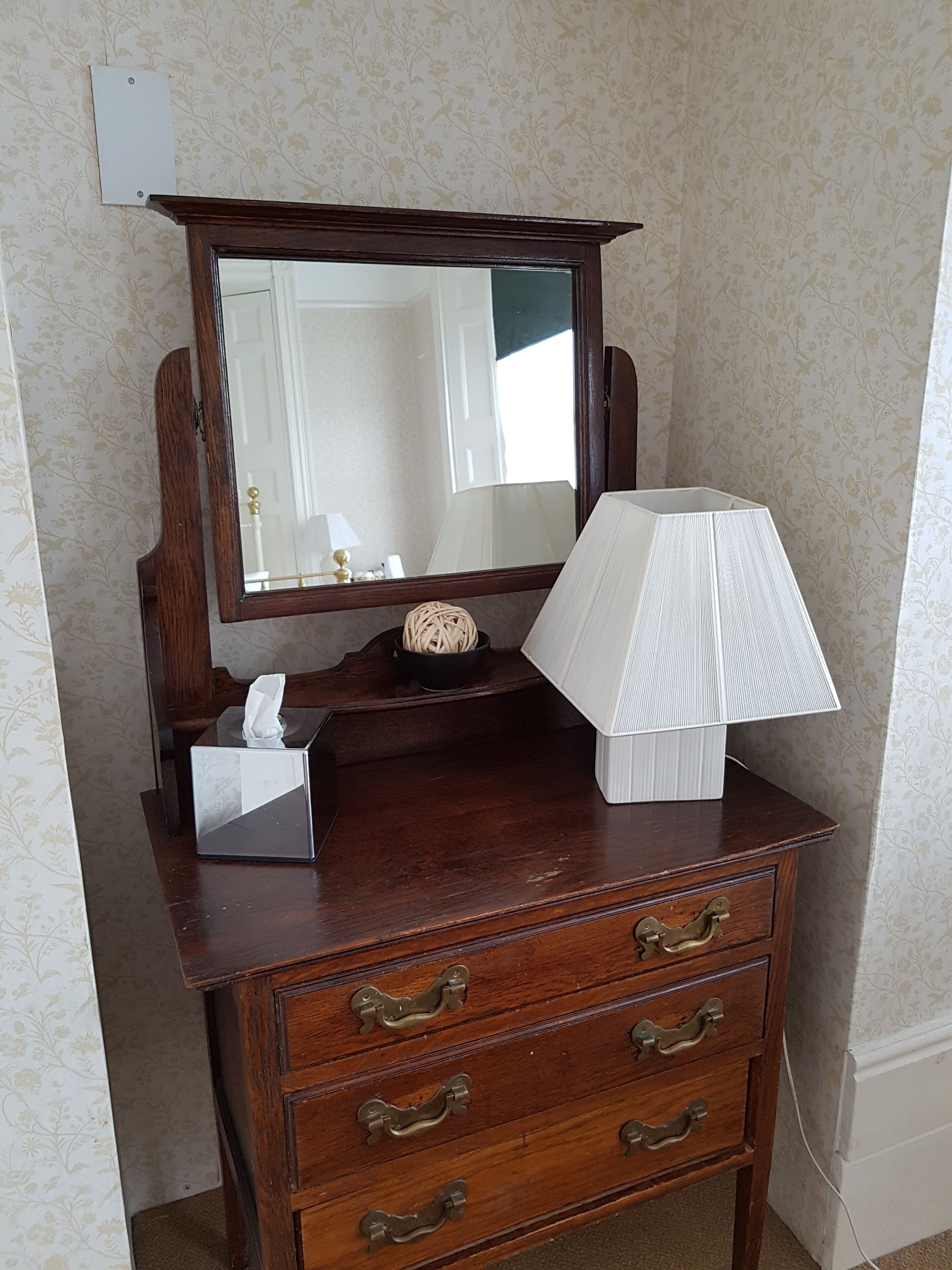 A wooden dresser with a mirror, a tissue box, and a lamp.