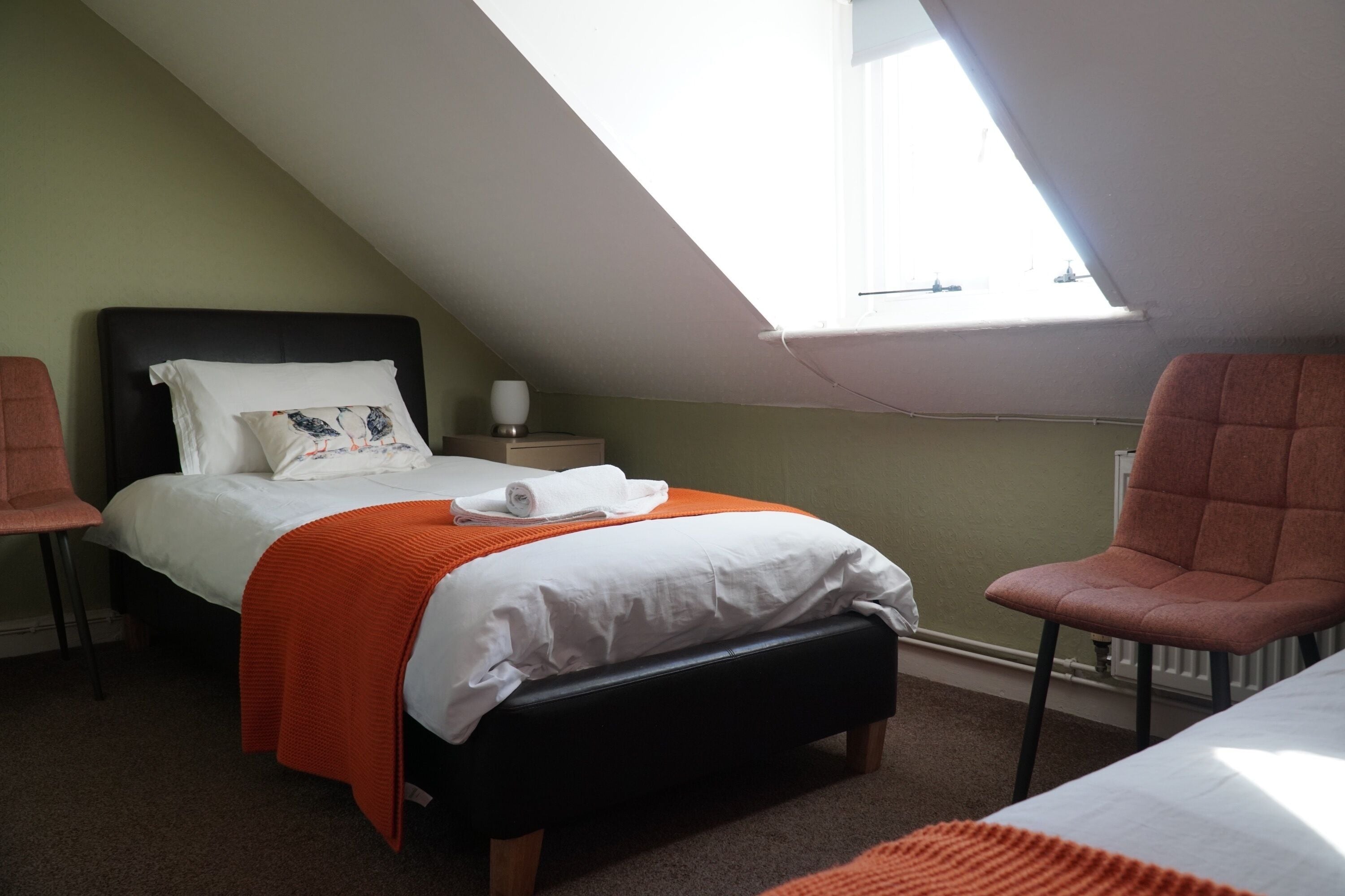 Une chambre à coucher avec un lit, une table de chevet, une chaise et une fenêtre.