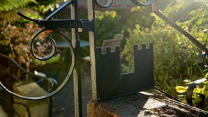 A metal gate with a castle-like design, set in a garden with greenery and a building in the background. - Castle Guest House (Dover)