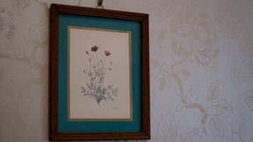 Una il·lustració botànica emmarcada a la paret, amb un fons de paper pintat amb un motiu floral.