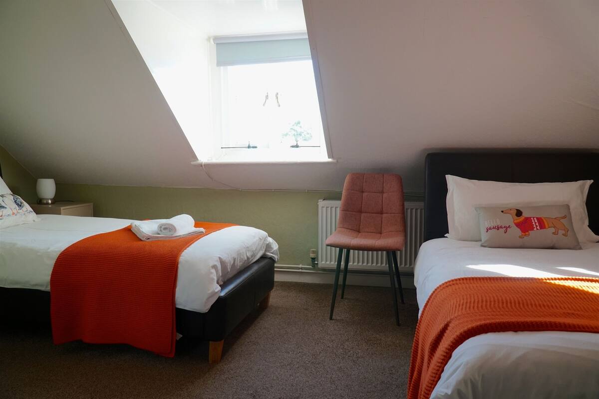 A bedroom with two beds, a window, a radiator, and a chair.