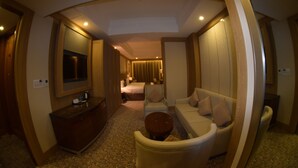Habitación de hotel con una cama grande, zona de estar con sofá y sillones, una mesita y un tocador con espejo, y un baño visible al fondo.