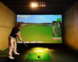 A golfer in a virtual golf simulation room with a large screen displaying a golf course.