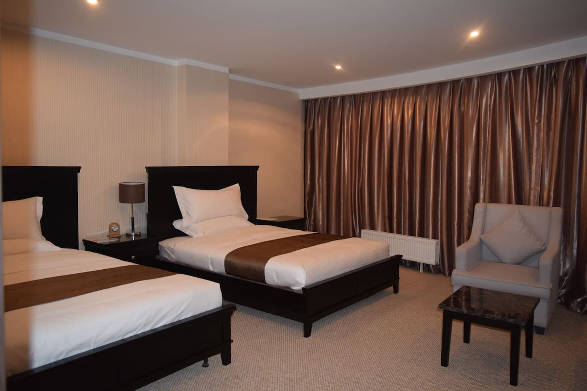 A hotel room with two beds, a chair, a small table, and a large window with curtains.
