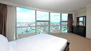 Habitación de hotel con una cama grande, un aparador y vistas de la ciudad a través de amplias ventanas.