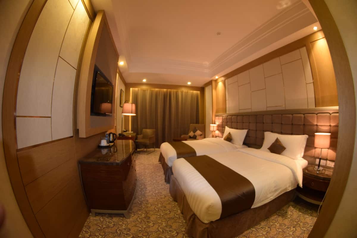 A hotel room with two beds, a desk, a chair, and a television.