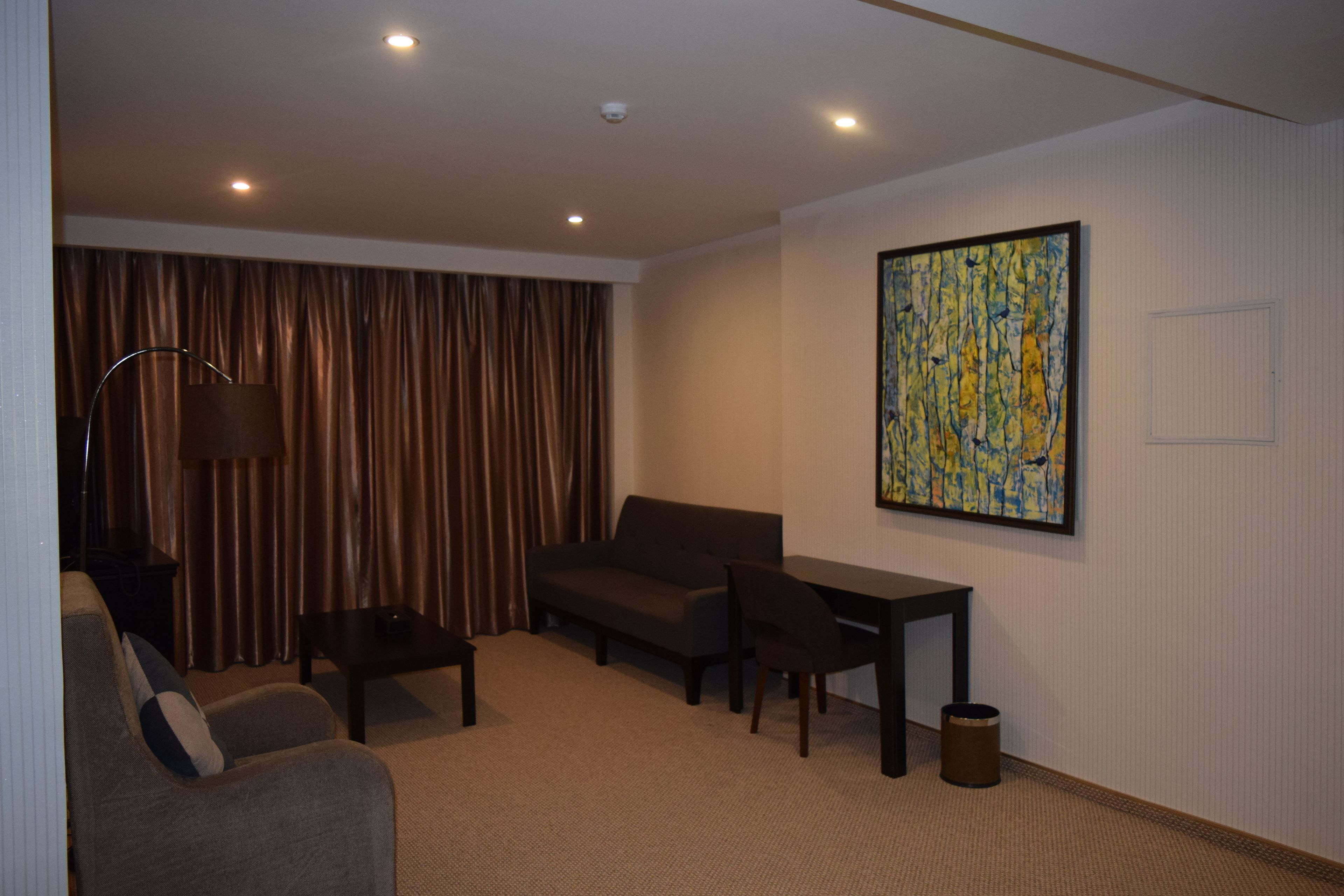 Ein modernes Hotelzimmer mit Sofa, Sesseln, einem kleinen Tisch und einem Gemälde an der Wand.
