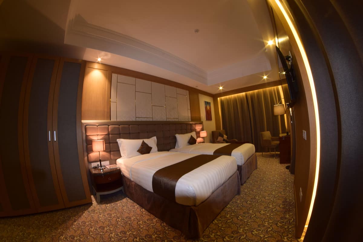 A hotel room with two beds, a large wardrobe, a desk, and a chair.