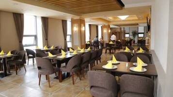 A hotel dining area with multiple tables and chairs, arranged in a spacious layout.