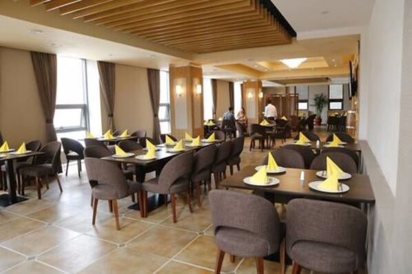A hotel dining area with multiple tables and chairs, arranged in a spacious layout.